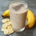 Vaso de batido de plátano, avena y chía servido frío, sobre fondo de madera natural
