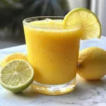 Jugo de limón con piña y zanahoria servido en vaso transparente, con rodaja de limón y hojas de menta