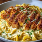 Plato servido con pechuga de pollo crujiente sobre pasta cremosa al ajo y parmesano