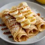Crepas de avena con plátano servidas con rodajas de fruta y yogur