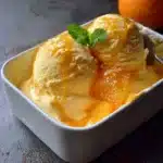 Helado casero de naranja cremoso servido en un bol con rodajas de naranja fresca