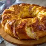 Rosca de jamón de pollo y queso recién horneada, dorada y esponjosa sobre una bandeja de madera.