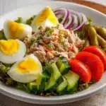 Plato servido de ensalada fresca con atún, huevo duro, lechuga, jitomate, pepino y zanahoria en un bol blanco.